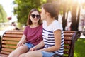 Two creative girls talk and laugh while sitting on bench outdoors. Young and funloving friends share ideas, thoughts and plan new Royalty Free Stock Photo