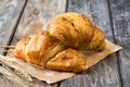 Two croissants with nuts on baking paper and spikelets, wooden background