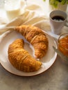 Two croissants on a white earthenware plate. An amber orange jam in a glass bowl and a cup of aromatic black coffee sit on a table Royalty Free Stock Photo