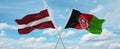 two crossed flags Afghanistan and Latvia waving in wind at cloudy sky. Concept of relationship, dialog, travelling between two