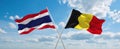 two crossed flags Belgium and Thailand waving in wind at cloudy sky. Concept of relationship, dialog, travelling between two