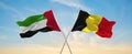 two crossed flags Belgium and United Arab Emirates waving in wind at cloudy sky. Concept of relationship, dialog, travelling