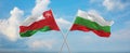 two crossed flags Bulgaria and Oman waving in wind at cloudy sky. Concept of relationship, dialog, travelling between two