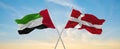 two crossed flags denmark and United Arab Emirates waving in wind at cloudy sky. Concept of relationship, dialog, travelling