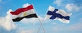 two crossed flags Finland and Egypt waving in wind at cloudy sky. Concept of relationship, dialog, travelling between two