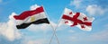 two crossed flags Georgia and Egypt waving in wind at cloudy sky. Concept of relationship, dialog, travelling between two