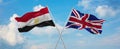 two crossed flags Great Britain and Egypt waving in wind at cloudy sky. Concept of relationship, dialog, travelling between two