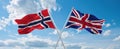 two crossed flags Great Britain and Norway waving in wind at cloudy sky. Concept of relationship, dialog, travelling between two