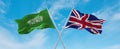 two crossed flags Great Britain and Saudi Arabia waving in wind at cloudy sky. Concept of relationship, dialog, travelling between