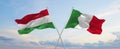 two crossed flags Hungary and Italy waving in wind at cloudy sky. Concept of relationship, dialog, travelling between two