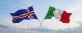 two crossed flags Iceland and Italy waving in wind at cloudy sky. Concept of relationship, dialog, travelling between two