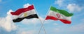 two crossed flags Iran and Egypt waving in wind at cloudy sky. Concept of relationship, dialog, travelling between two countries