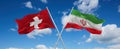 two crossed flags Iran and Switzerland waving in wind at cloudy sky. Concept of relationship, dialog, travelling between two