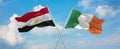 two crossed flags Ireland and Egypt waving in wind at cloudy sky. Concept of relationship, dialog, travelling between two