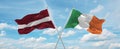 two crossed flags Ireland and Latvia waving in wind at cloudy sky. Concept of relationship, dialog, travelling between two