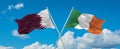 two crossed flags Ireland and Qatar waving in wind at cloudy sky. Concept of relationship, dialog, travelling between two