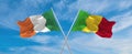 two crossed flags Mali and Ireland waving in wind at cloudy sky. Concept of relationship, dialog, travelling between two countries