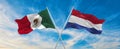 two crossed flags Mexico and Netherland waving in wind at cloudy sky. Concept of relationship, dialog, travelling between two