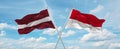 two crossed flags Monaco and Latvia waving in wind at cloudy sky. Concept of relationship, dialog, travelling between two