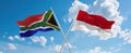 two crossed flags Monaco and South Africa waving in wind at cloudy sky. Concept of relationship, dialog, travelling between two