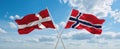 two crossed flags Norway and Denmark waving in wind at cloudy sky. Concept of relationship, dialog, travelling between two