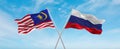 two crossed flags Russia and Malaysia waving in wind at cloudy sky. Concept of relationship, dialog, travelling between two