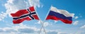 two crossed flags Russia and Norway waving in wind at cloudy sky. Concept of relationship, dialog, travelling between two