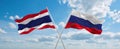 two crossed flags Russia and Thailand waving in wind at cloudy sky. Concept of relationship, dialog, travelling between two