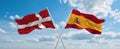 two crossed flags Spain and Denmark waving in wind at cloudy sky. Concept of relationship, dialog, travelling between two