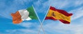 two crossed flags Spain and Ireland waving in wind at cloudy sky. Concept of relationship, dialog, travelling between two
