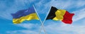 two crossed flags Ukraine and Belgium waving in wind at cloudy sky. Concept of relationship, dialog, travelling between two