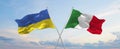two crossed flags Ukraine and Italy waving in wind at cloudy sky. Concept of relationship, dialog, travelling between two