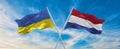 two crossed flags Ukraine and Netherland waving in wind at cloudy sky. Concept of relationship, dialog, travelling between two