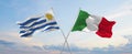 two crossed flags Uruguay and Italy waving in wind at cloudy sky. Concept of relationship, dialog, travelling between two