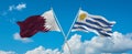 two crossed flags Uruguay and Qatar waving in wind at cloudy sky. Concept of relationship, dialog, travelling between two