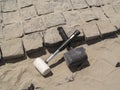 Two crossed rubber hammers lie on the unfinished laying of granite paving stones