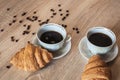 Two cup of hot coffee in a plate and a croissants, coffee beans are scattered on a table Royalty Free Stock Photo