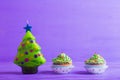 Two cupcakes with creamy green top and candle in form of Christmas tree on purple background. Royalty Free Stock Photo