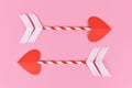 Two cupid love arrow with heart shaped tip made from paper on pink background