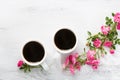 Two cups of black coffee and branch of small pink roses.