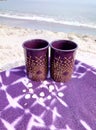 Two cups on a blanket on the beach.