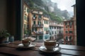 Two cups of capuccino coffee on on a windowsill overlooking typical italian town on a rainy day