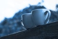 Two cups of coffee in classic blue color of the Year 2020 on wooden balcony on the background of sunset with bokeh light Royalty Free Stock Photo