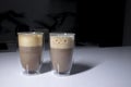 Two cups of coffee in double-botoom glass on white table in gray kitchen