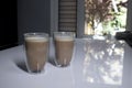 Two cups of coffee in double-botoom glass on white table in gray kitchen