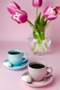 A two cups of coffee and a glass vase with pink tulips on the pink background. Close-up Royalty Free Stock Photo