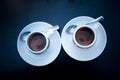 Two cups of coffee with round white plates and tea spoons on black table. View from above. Morning coffee in bar for a Royalty Free Stock Photo