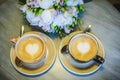 Two cups of coffee stand on the table against bouquet of flowers