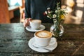 Two cups of coffee and a vase of flowers on a wooden table, the girl holds in her hand one cup of coffee in the Royalty Free Stock Photo