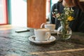 Two cups of coffee and a vase of flowers on a wooden table, the girl holds in her hand one cup of coffee in the Royalty Free Stock Photo